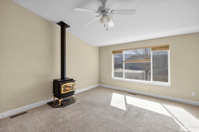 unfurnished living room with visible vents, carpet flooring, a wood stove, and baseboards