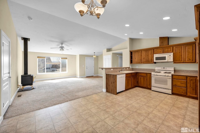 kitchen featuring open floor plan, light carpet, a peninsula, a wood stove, and white appliances