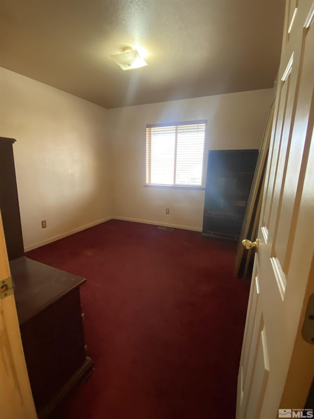 spare room featuring dark carpet and baseboards