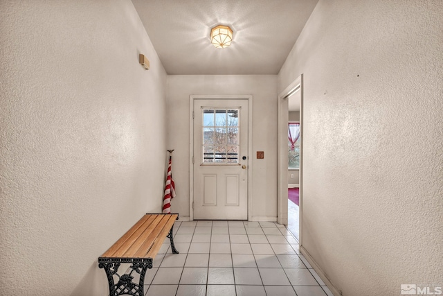 doorway to outside featuring light tile patterned floors, baseboards, and a textured wall