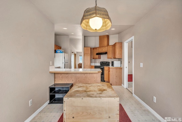 kitchen with baseboards, a peninsula, freestanding refrigerator, under cabinet range hood, and black electric range oven