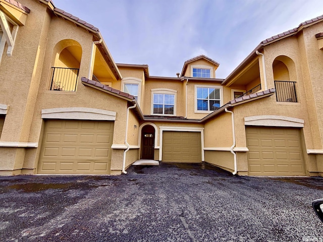 townhome / multi-family property featuring stucco siding, driveway, an attached garage, and a tile roof