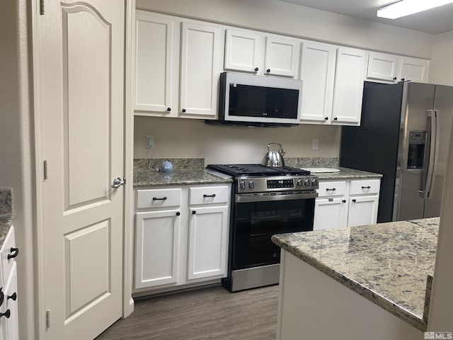 kitchen with white cabinets, light stone countertops, wood finished floors, and appliances with stainless steel finishes