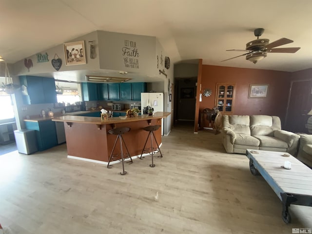 kitchen featuring blue cabinets, freestanding refrigerator, a breakfast bar area, light wood finished floors, and lofted ceiling