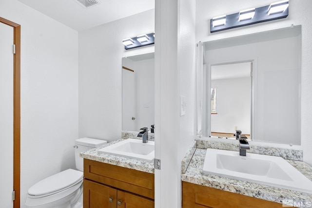 bathroom featuring two vanities, toilet, visible vents, and a sink