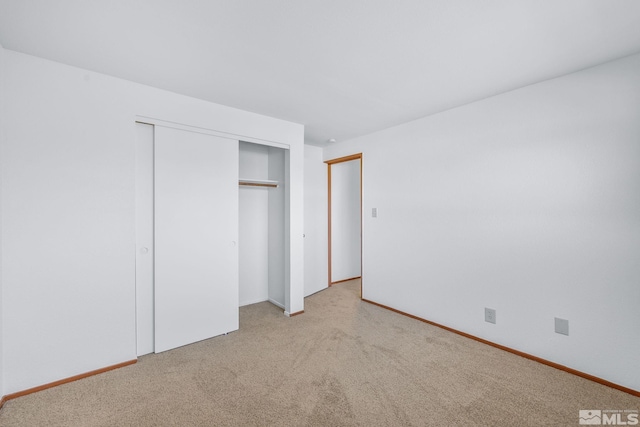 unfurnished bedroom with a closet, light colored carpet, and baseboards