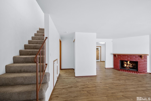 interior space with stairway, baseboards, a brick fireplace, and wood finished floors