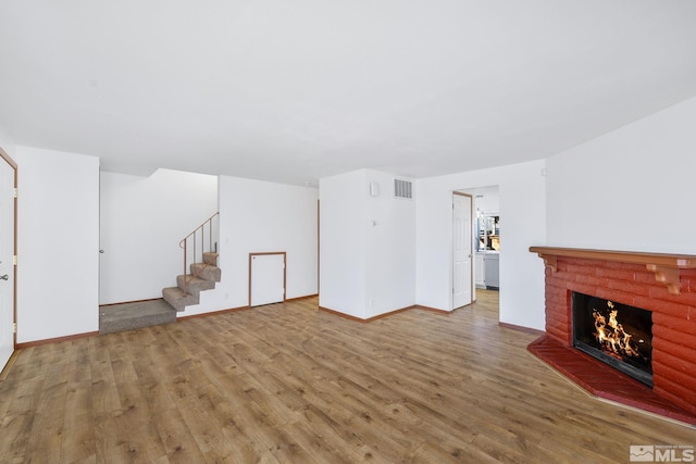 unfurnished living room featuring stairs, wood finished floors, baseboards, and a fireplace