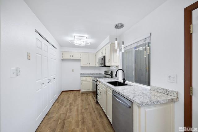 kitchen featuring light wood-style floors, hanging light fixtures, white cabinets, stainless steel appliances, and a sink