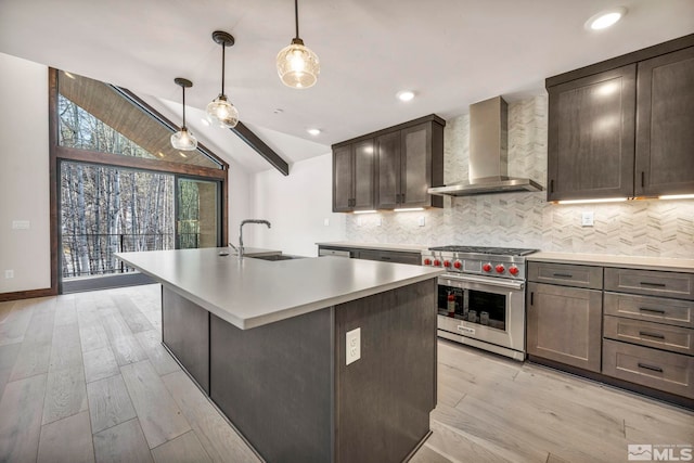 kitchen with a sink, tasteful backsplash, premium stove, wall chimney range hood, and lofted ceiling