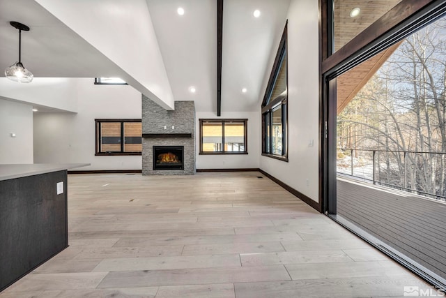 unfurnished living room with light wood-type flooring, beam ceiling, a large fireplace, and baseboards