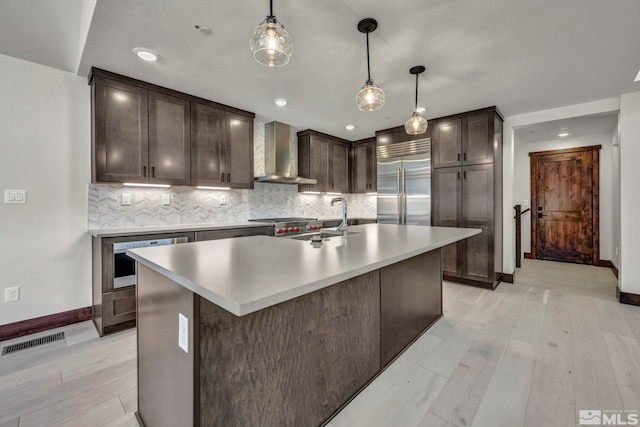 kitchen featuring visible vents, wall chimney range hood, dark brown cabinetry, built in refrigerator, and a sink