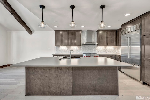 kitchen featuring backsplash, built in fridge, stove, wall chimney exhaust hood, and a sink