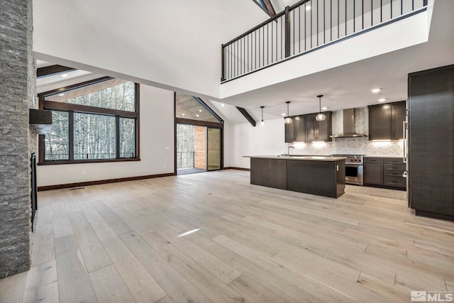 kitchen with light wood-style floors, a towering ceiling, high end stainless steel range oven, wall chimney range hood, and open floor plan