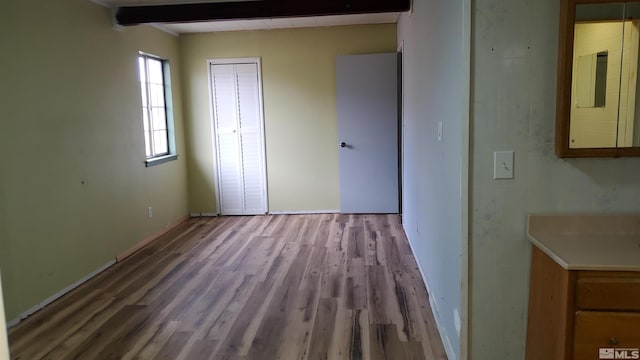 unfurnished bedroom featuring beam ceiling, a closet, and wood finished floors