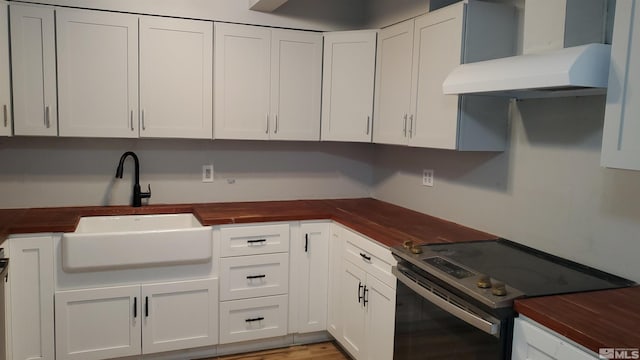 kitchen featuring wooden counters, wall chimney range hood, electric range, white cabinets, and a sink