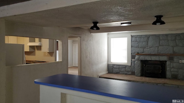 kitchen with freestanding refrigerator, a fireplace, a textured ceiling, and wall chimney exhaust hood