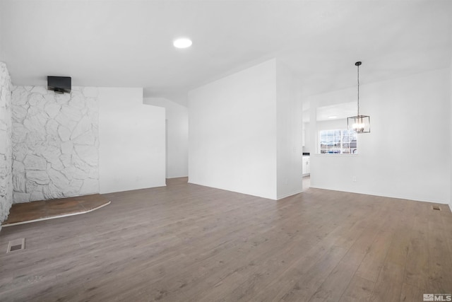 unfurnished living room featuring visible vents, an inviting chandelier, and wood finished floors