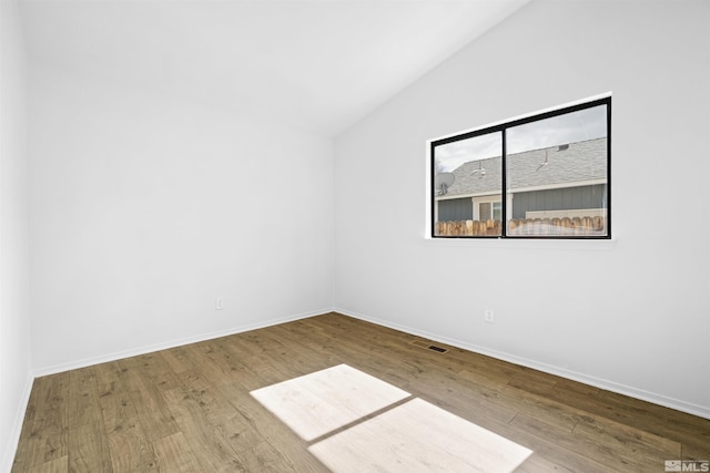 unfurnished room featuring visible vents, baseboards, lofted ceiling, and wood finished floors