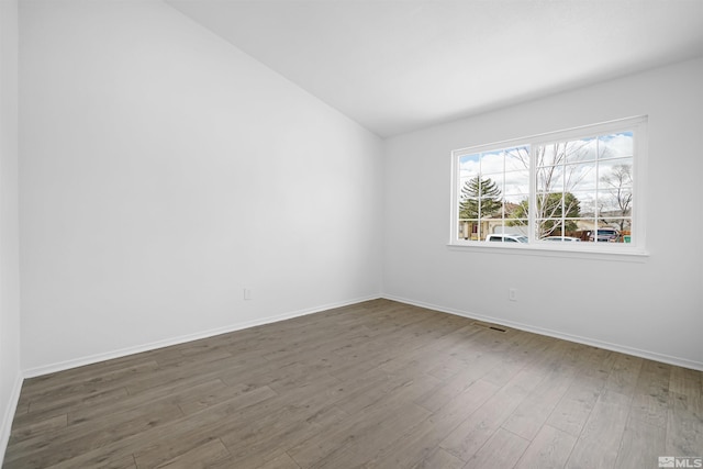 empty room featuring vaulted ceiling, wood finished floors, visible vents, and baseboards