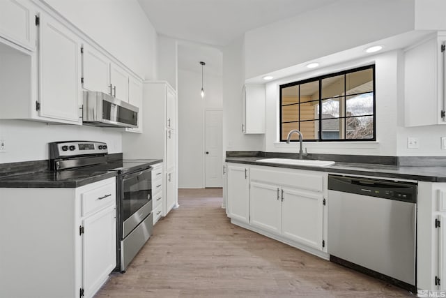 kitchen with light wood finished floors, a sink, white cabinets, appliances with stainless steel finishes, and dark countertops