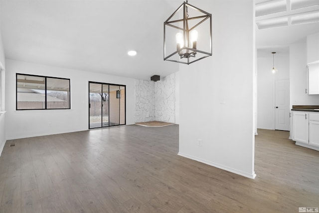 empty room with a notable chandelier, baseboards, and wood finished floors