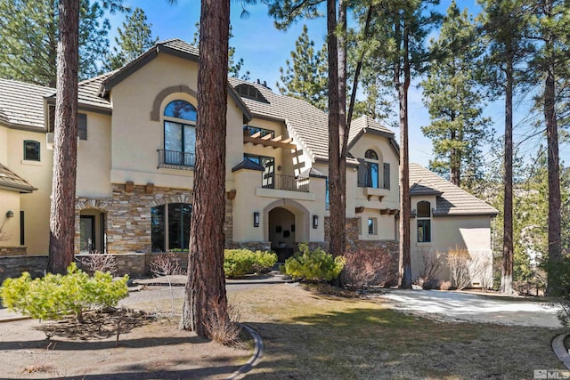 view of front facade with stucco siding, stone siding, a balcony, and a tiled roof