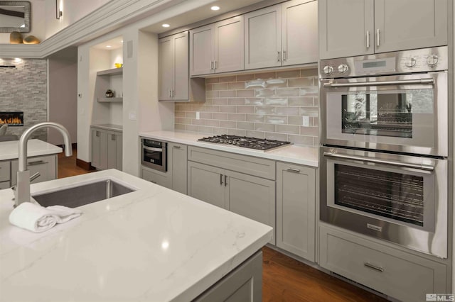 kitchen featuring gray cabinets, a sink, backsplash, appliances with stainless steel finishes, and a fireplace