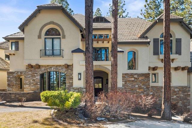 view of front facade with a balcony, stone siding, and stucco siding