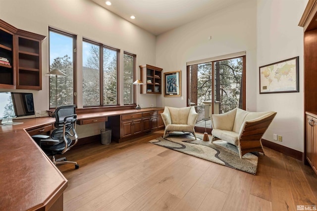 home office with baseboards, built in study area, light wood-style flooring, recessed lighting, and a towering ceiling