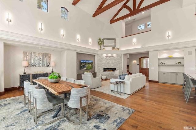 dining space with beamed ceiling, built in features, wood finished floors, a large fireplace, and arched walkways