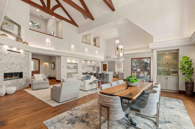 dining room featuring built in shelves, high vaulted ceiling, beam ceiling, wood finished floors, and a large fireplace