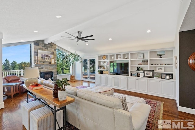 living area featuring wood finished floors, baseboards, vaulted ceiling with beams, a fireplace, and ceiling fan