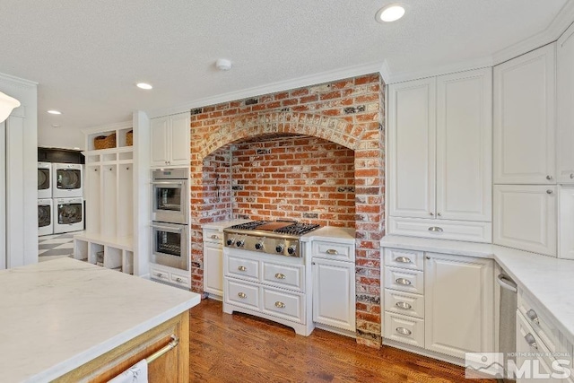 kitchen with wood finished floors, stainless steel appliances, a textured ceiling, white cabinetry, and stacked washer / dryer