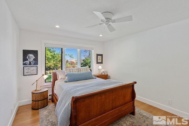 bedroom featuring light wood finished floors, ceiling fan, a textured ceiling, and baseboards