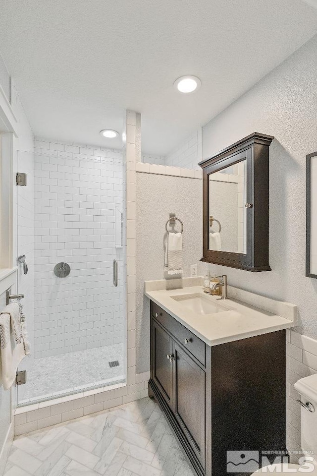 bathroom featuring toilet, marble finish floor, a textured ceiling, a shower stall, and vanity