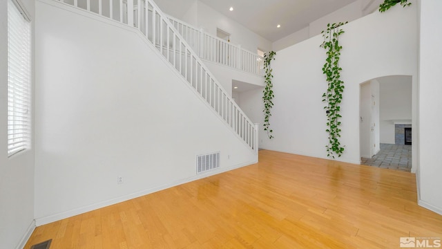 spare room with visible vents, a fireplace, a high ceiling, wood finished floors, and arched walkways