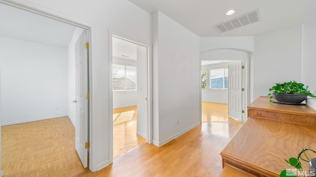 hall with a wealth of natural light, visible vents, arched walkways, and parquet floors