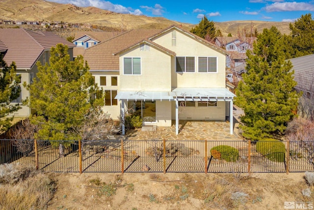 view of front of house with a tiled roof, stucco siding, a fenced backyard, a patio area, and a mountain view