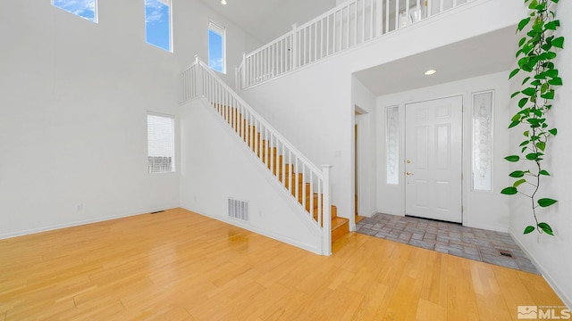 entrance foyer with visible vents, baseboards, stairway, a high ceiling, and wood finished floors