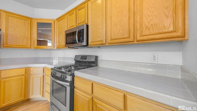 kitchen featuring appliances with stainless steel finishes, glass insert cabinets, and tile counters