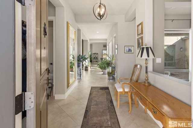 hall featuring light tile patterned floors, a chandelier, and baseboards