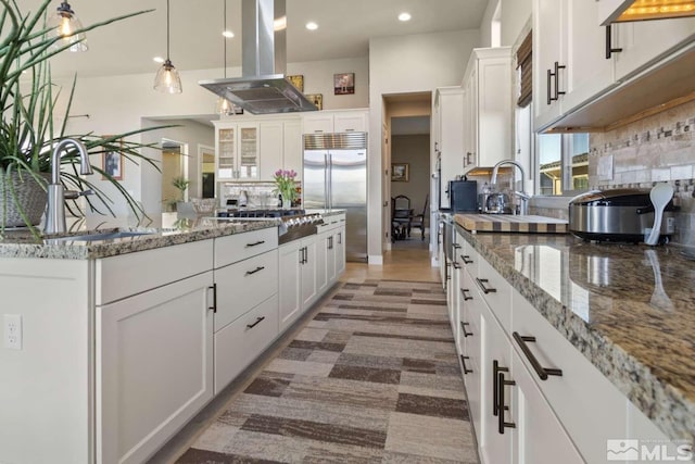 kitchen with island exhaust hood, a sink, backsplash, white cabinetry, and stainless steel appliances