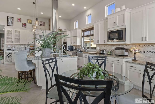 kitchen featuring tasteful backsplash, stainless steel microwave, a center island with sink, and white cabinets