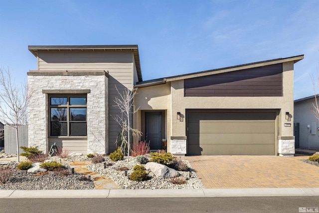 modern home with decorative driveway, stone siding, an attached garage, and stucco siding