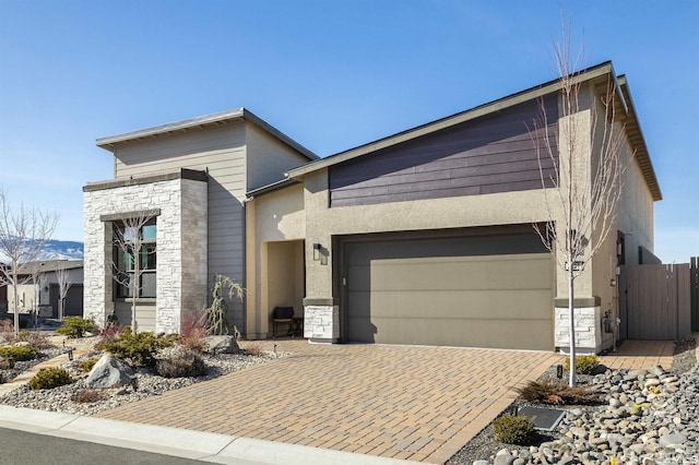 contemporary house featuring decorative driveway, an attached garage, stone siding, and stucco siding