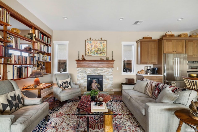 living room with wood finished floors, visible vents, baseboards, recessed lighting, and a glass covered fireplace