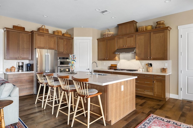 kitchen featuring visible vents, dark wood-type flooring, a sink, under cabinet range hood, and stainless steel appliances