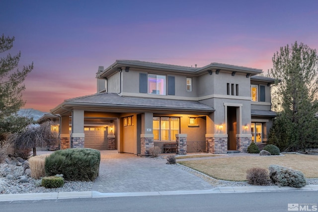 prairie-style house featuring decorative driveway, stone siding, a porch, and stucco siding