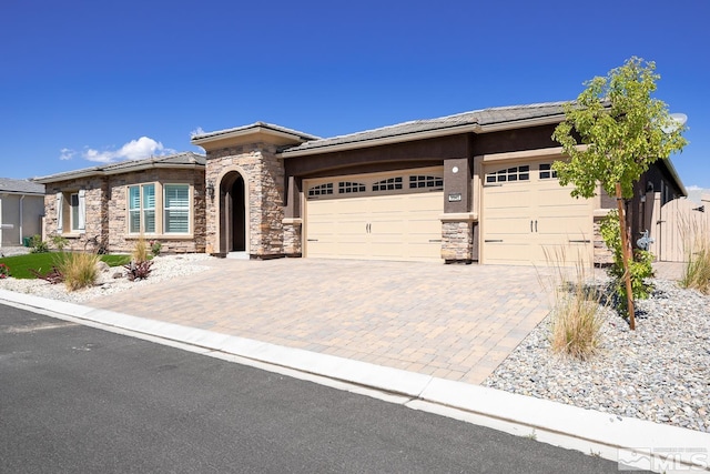 prairie-style home featuring a tile roof, stucco siding, decorative driveway, stone siding, and an attached garage